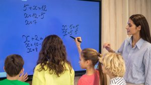children-writing-blackboard-attentive-teacher-watching